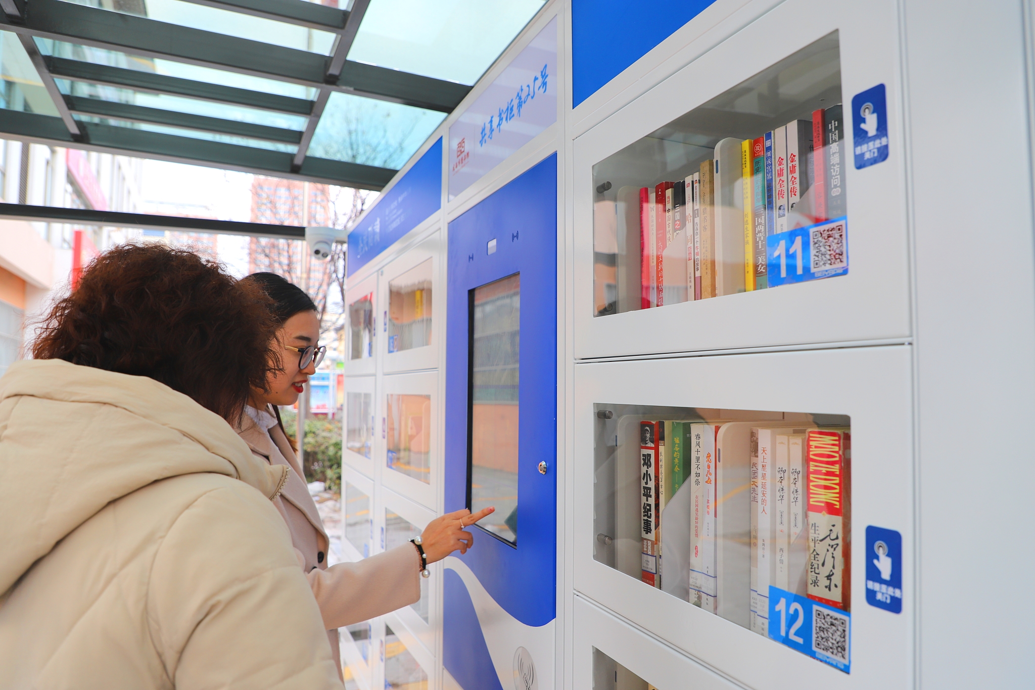 中心门口南侧共享书柜处,几名手拿借书卡的市民正在排队等候借阅图书